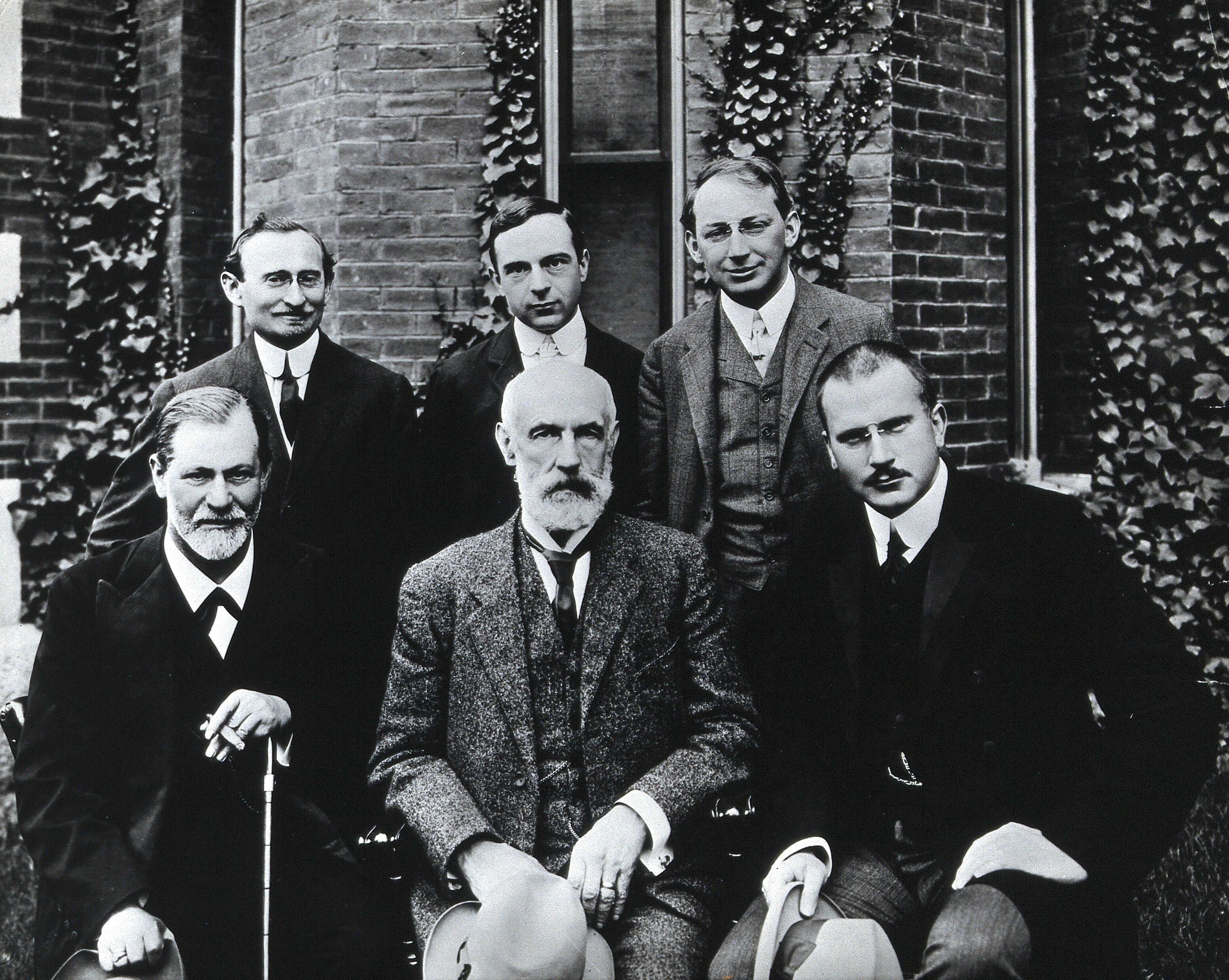 Retrato histórico de seis homens diante de um edifício; Freud, Hall e Jung estão sentados na primeira fila.